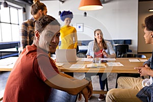 Portrait of caucasian male creative in casual office meeting with diverse colleagues using laptop