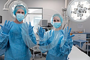 Portrait of caucasian male and female surgeons standing in operating theatre wearing face mask