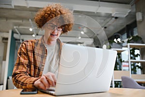 Portrait of Caucasian male freelancer in trendy apparel sitting at cafeteria table and doing remote work for programming