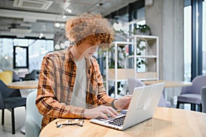 Portrait of Caucasian male freelancer in trendy apparel sitting at cafeteria table and doing remote work for programming