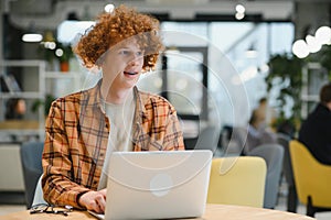 Portrait of Caucasian male freelancer in trendy apparel sitting at cafeteria table and doing remote work for programming