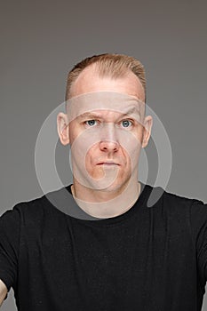 portrait of caucasian man in black t-shirt looks to the camera with a doubt isolated on grey background