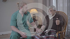 Portrait of Caucasian man listening to stories of upset retiree in nursing home and holding his hand. Male nurse