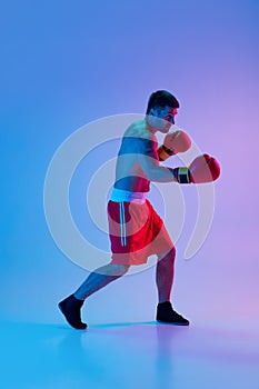 Portrait of Caucasian man, professional boxer in sportwear boxing on studio background in gradient neon light. Concept