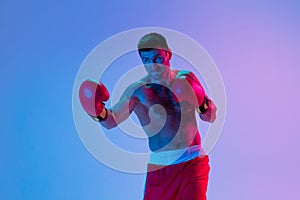 Portrait of Caucasian man, professional boxer in sportwear boxing on studio background in gradient neon light. Concept