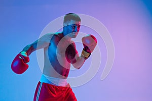 Portrait of Caucasian man, professional boxer in sportwear boxing on studio background in gradient neon light. Concept
