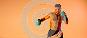 Portrait of Caucasian man, professional boxer in sportwear boxing on studio background in yellow neon light. Concept of