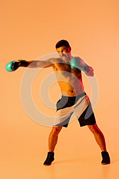 Portrait of Caucasian man, professional boxer in sportwear boxing on studio background in yellow neon light. Concept of