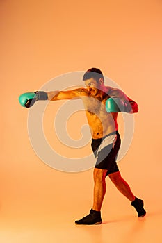 Portrait of Caucasian man, professional boxer in sportwear boxing on studio background in yellow neon light. Concept of