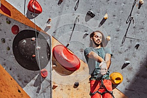 Portrait of Caucasian man professional rock climber warms-up at front of climbing wall at training center in sunny day
