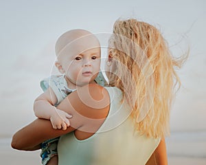 Portrait of Caucasian mother with blond hair and baby son spending time on beach. Summer vacation in Asia. Family relationships.
