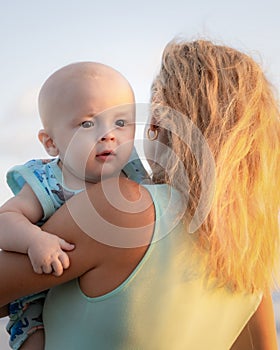 Portrait of Caucasian mother with blond hair and baby son spending time on beach. Summer vacation in Asia. Family relationships.