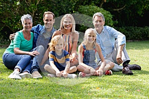 Portrait of caucasian parents, grandparents and grandchildren sitting in garden smiling to camera