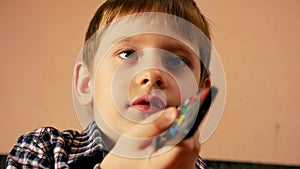 Portrait of Caucasian preschool boy holding TV remote control. The child switches television channels. The kid is watching tv. Sel