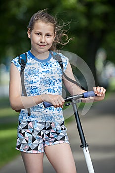 Portrait of Caucasian preteen girl with wheel of kick scooter in hands, outdoor