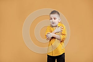 portrait of caucasian scared child boy on yellow background. amazed stressed boy in yellow shirt. school child afraid or