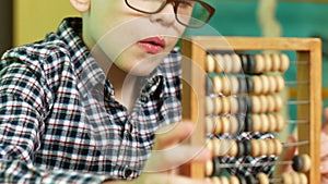 Portrait of a Caucasian schoolboy 7-8 years old wearing glasses counting on wooden abacus. The topic of education and learning mat