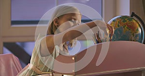 Portrait of Caucasian schoolgirl looking at globe and writing down something. Intelligent child doing homework at home