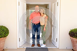 Portrait of caucasian senior couple smiling while standing on the front door of their house