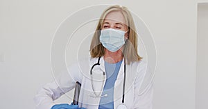 Portrait of caucasian senior female doctor wearing surgical gloves and face mask using tablet comput
