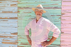 Portrait of caucasian senior man wearing hat with hands on hip standing against wooden wall