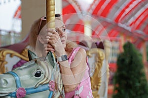 Portrait of Caucasian senior woman ride horse on Carousel at amusement park with lonely mood