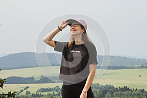 Portrait of caucasian smiling woman in black t-shirt and cap enjoying of view on mountain top. Happy hiking.