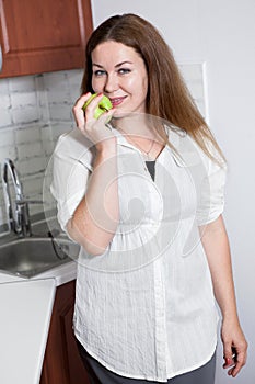 Portrait of Caucasian smiling woman with a green tasty apple, domestic kitchen