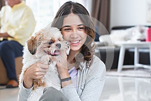 Portrait of Caucasian teenage girl playing with shih tzu puppy dog at home. Young beautiful woman sitting on floor, smiling,