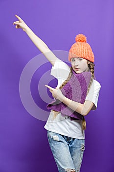 Portrait of Caucasian Teenager Girl in Coral Warm Knitted Winter Hat and Violet Scarf Showing Direction With Both Hands Over