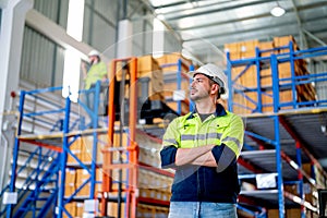 Portrait of Caucasian warehouse worker stand with arm-crossed and look to left side in front of co-worker work and manage boxes on