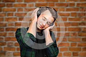 Portrait of a caucasian White young guy listen music in the ear-phones with eyes closed. Handsome man dressed in a black T-shirt