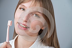 Portrait of a caucasian woman with braces on her teeth holding a toothbrush.