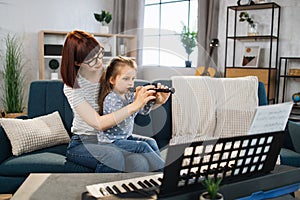 Portrait of caucasian woman and her cute little daughter learning to play flute at home.