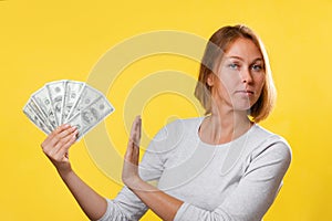 Portrait of a caucasian woman holding a fan of dollars in her hand, and refusing them. Yellow background. The concept of