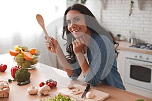 Portrait of caucasian woman holding spatula at the kitchen and smiling at the camera