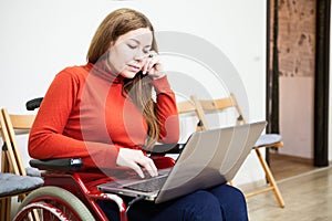 Portrait of Caucasian woman in invalid wheel-chair working with laptop on knees, disabled person