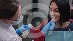 Portrait of Caucasian woman looking at hand mirror as dentist trying on implant. Close-up female patient and dentist