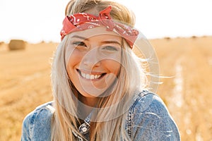 Portrait of caucasian woman 20s laughing and walking through golden field, during sunny day