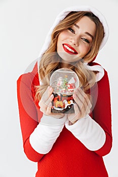 Portrait of caucasian woman 20s wearing Santa Claus red costume smiling and holding Christmas snow ball, isolated over white