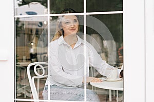 Portrait of a Caucasian woman in a stylish cafe sitting at a table with a smile while having coffee time. Girl relax