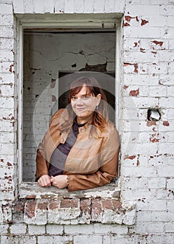 Portrait of a Caucasian Woman Wearing a Tan Leather Jacket Leaning Out the Window of an Old Brick Building