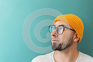 Portrait of a Caucasian young bearded man with glasses and a hat looking at the left side. Copy space. The concept of