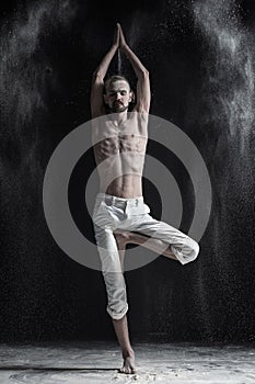 Portrait of caucasian young man wearing white sport pants doing yoga or pilates exercise.