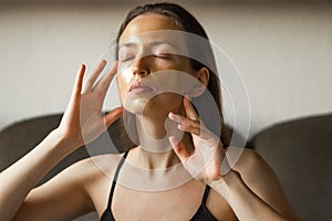 Portrait of caucasian young woman applying moisturizing or peeling golden facial mask and touch her face with hands.