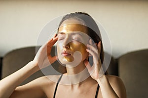 Portrait of caucasian young woman applying moisturizing or peeling golden facial mask and touch her face with hands.