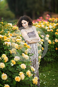 A portrait of Caucasian young woman near yellow roses bush in a rose garden, looking straight to the camera