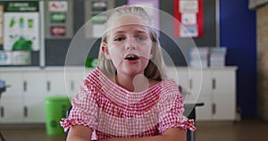 Portrait of causacian schoolgirl sitting at classroom, answering question, looking at camera