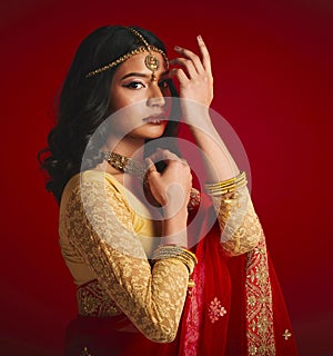 Portrait, celebration and Indian woman with fashion, traditional dress and jewellery against a red studio background