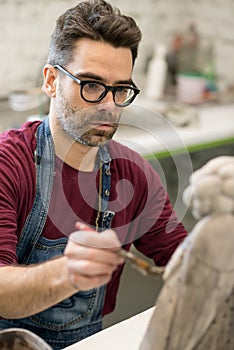 Portrait of Ceramist Dressed in an Apron Working on Clay Sculpture in Bright Ceramic Workshop. photo